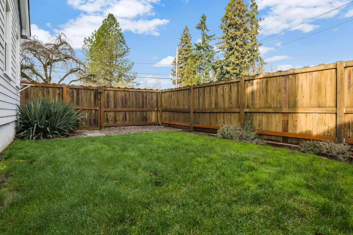 A tranquil green backyard with well-maintained grass, a sturdy wooden fence providing privacy and safety, and mature trees offering shade. The open lawn offers ample room for children or pets to play and for families to unwind outdoors.