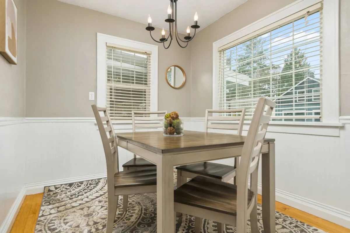 A bright dining space with a large table, elegant chandelier, decorative mirror, and window views. The area is seamlessly integrated with the overall flow of the open-concept layout, perfect for meals, work, or casual gatherings.