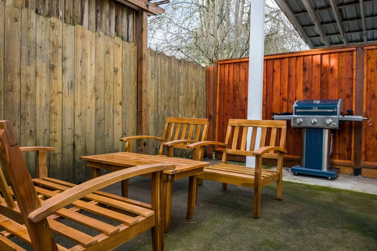 This image shows a friendly backyard scene featuring wooden chairs positioned around a grill, all bordered by a tall wooden fence. The setup evokes a sense of relaxed outdoor living and is ideal for socializing, playing outdoor games, or unwinding as the sun sets.