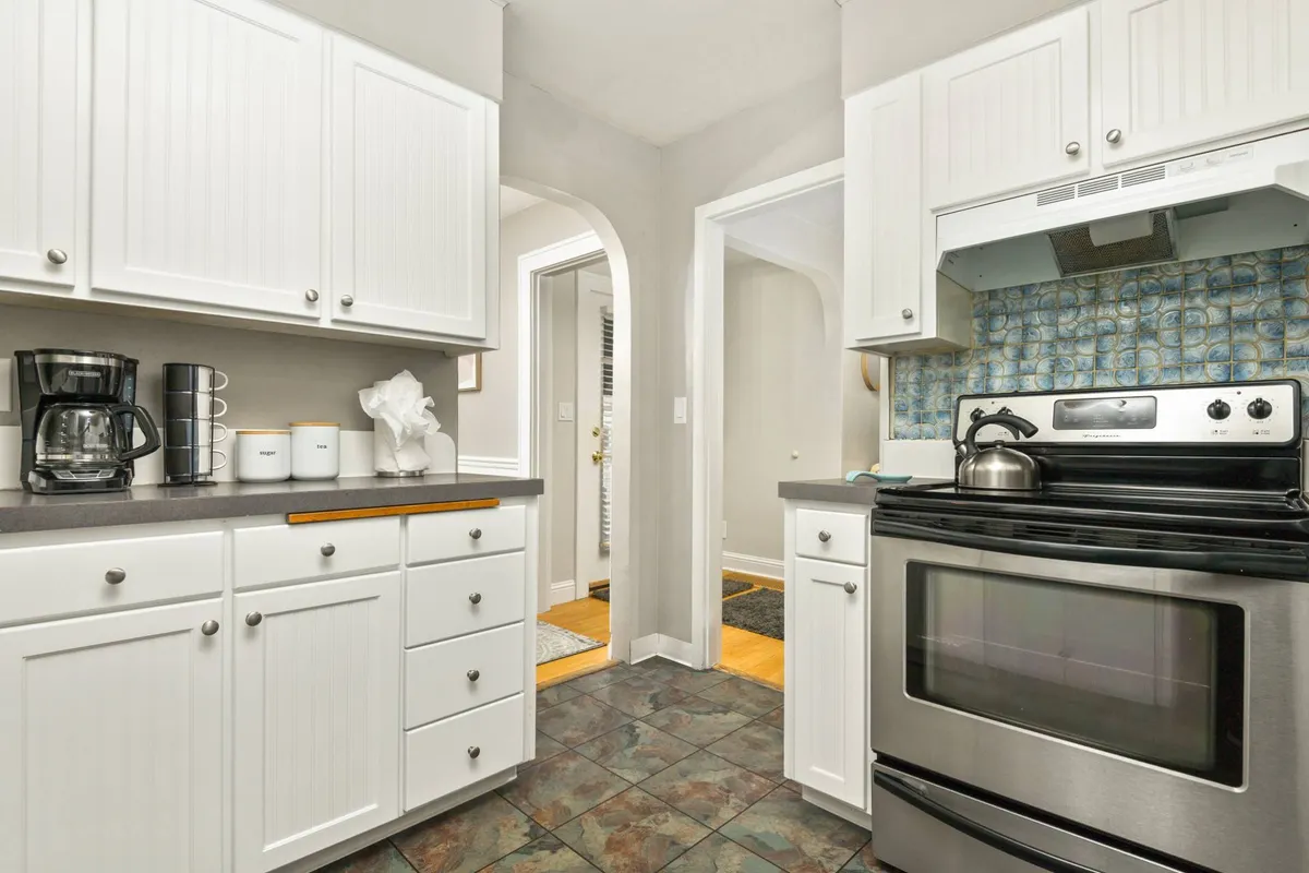 This image features a stylish kitchen with a stainless steel stove, blue backsplash, white cabinetry, and a coffee maker on the countertop. The scene evokes a sense of culinary possibility, with modern appliances and a cozy atmosphere conducive to meal preparation and socializing.