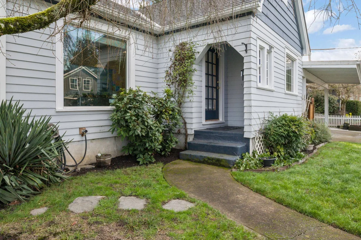 This exterior photo captures the welcoming front steps of Edwards Retreat, complemented by a landscaped garden and a large window. The scene hints at the walkable neighborhood setting, with space for guests to gather informally on the porch or for children to play outdoors.