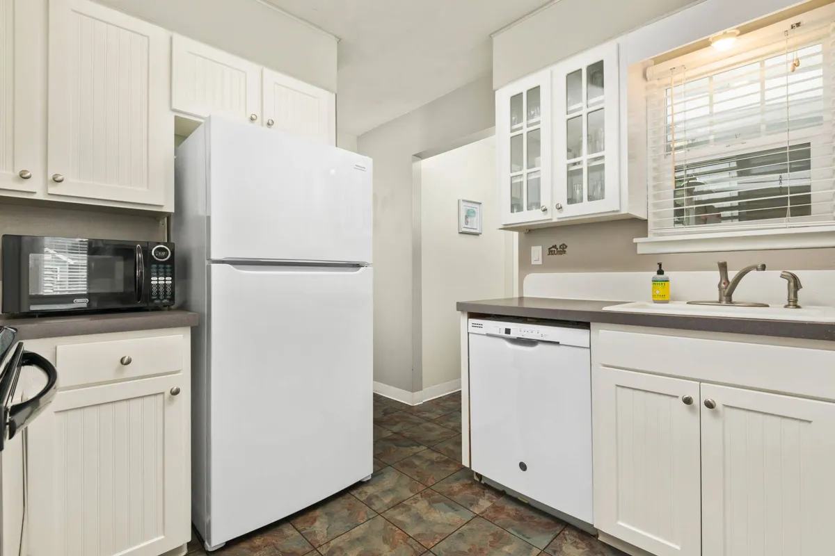 The image shows a bright kitchen area with a refrigerator, dishwasher, sink, and kitchen cabinets. The space is arranged for easy meal prep and gatherings, suggesting both functionality and warmth for family-style cooking.