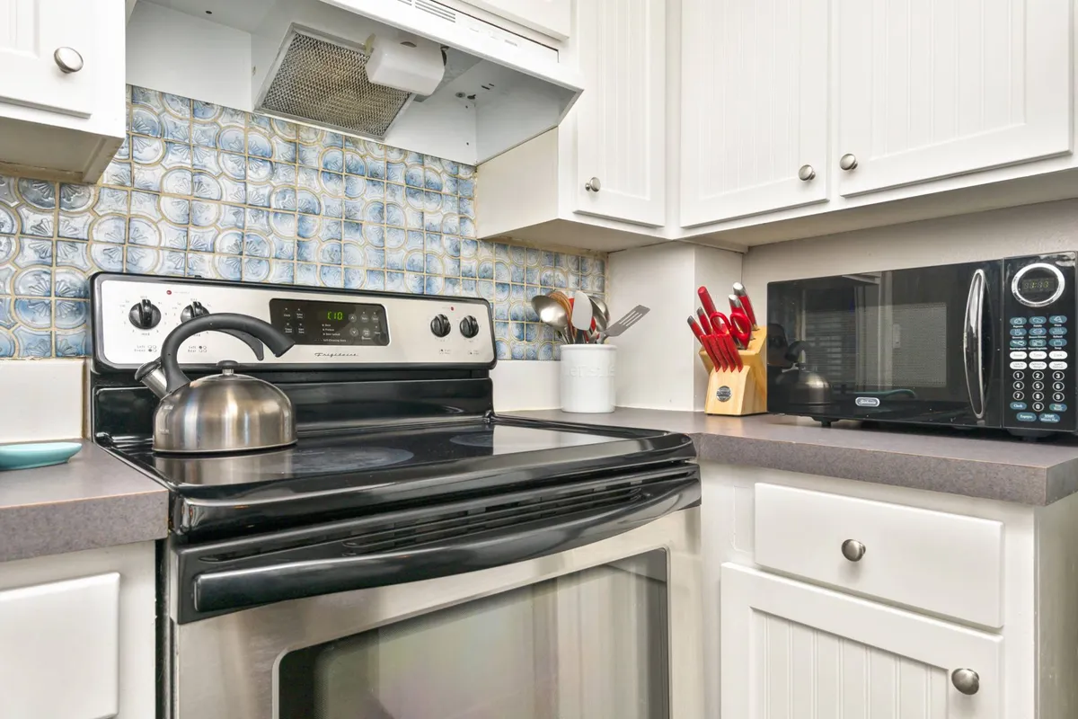 An inviting kitchen scene featuring a stove, kettle, kitchen utensils, and microwave set against textured backsplash tiles. The setup suggests a space well-equipped for meal preparation, entertaining, and trying new recipes, reinforcing the idea of home-cooked meals and casual gatherings.